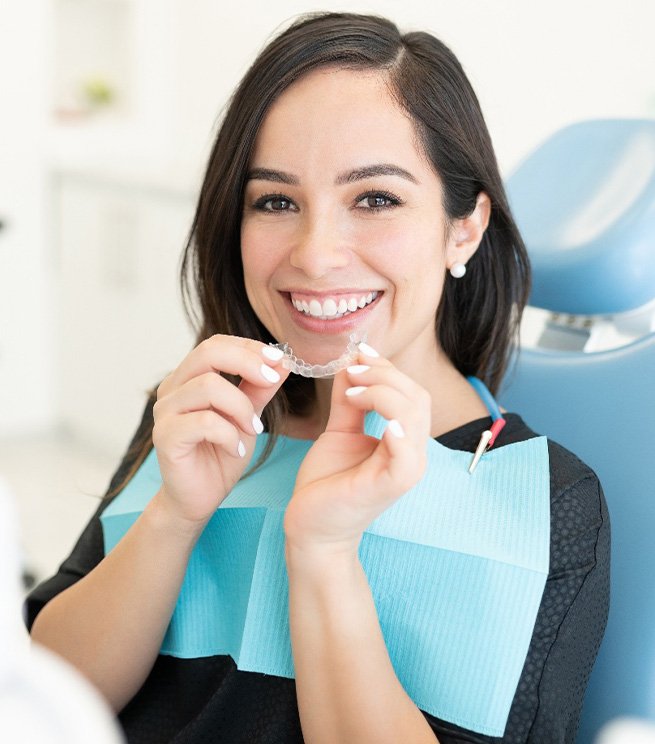 Smiling woman in dental chair holding clear aligner