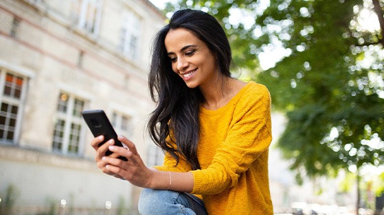 Woman smiling while looking at phone outside
