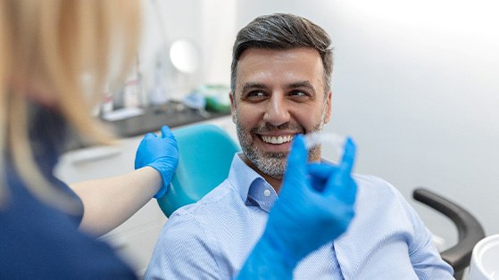 Man in dental chair smiling at dentist holding Invisalign