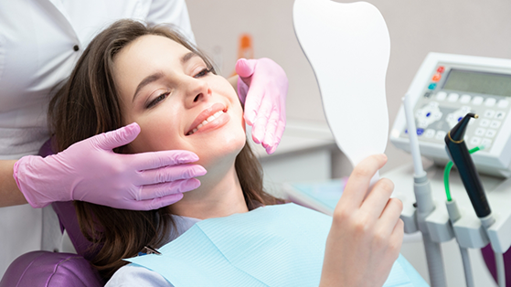 Young woman in the dental chair admiring her smile in a mirror