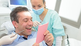 man smiling in dental chair while looking into a mirror