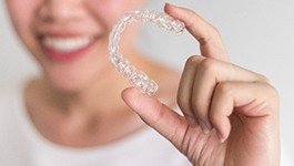 Smiling woman holding Invisalign clear aligner