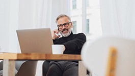 Man with glasses smiling while working on laptop