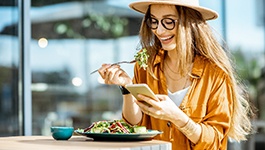 Smiling woman enjoying lunch while looking at phone