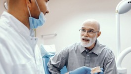 An older man speaking with a dentist.