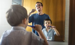 A father and son brushing their teeth.