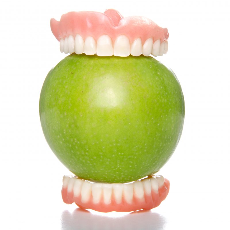 Close-up of dentures holding green apple