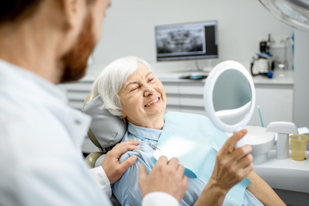 elderly patient smiling in mirror at dental appointment