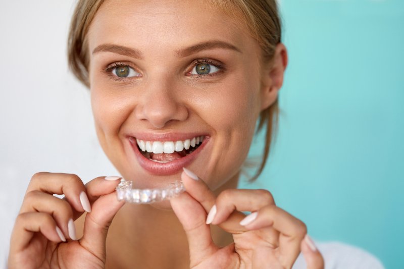 A blonde, smiling woman holding a teeth whitening tray