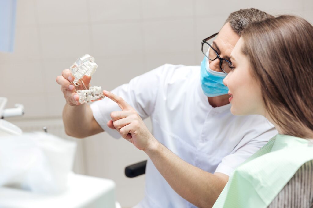 Dentist showing sample implant in clear jaw to patient