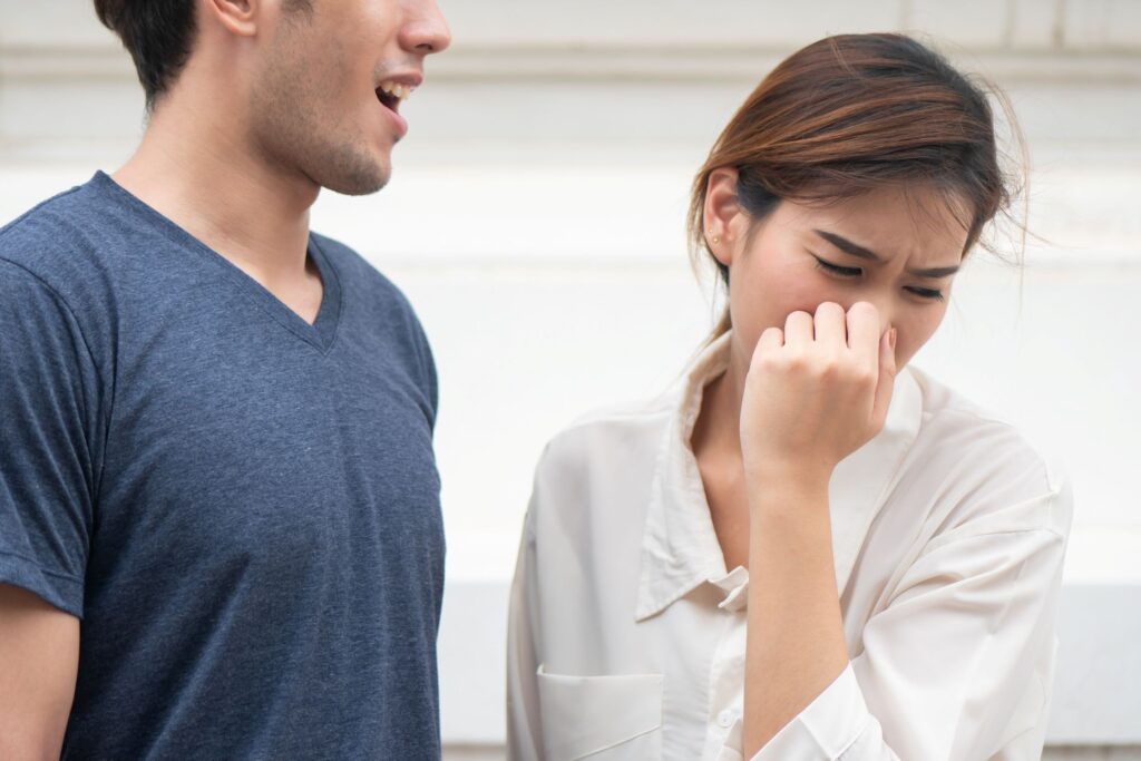 Woman turning head away from man with open mouth holding her nose closed