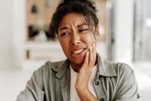 Woman with sensitive teeth wincing and holding mouth.